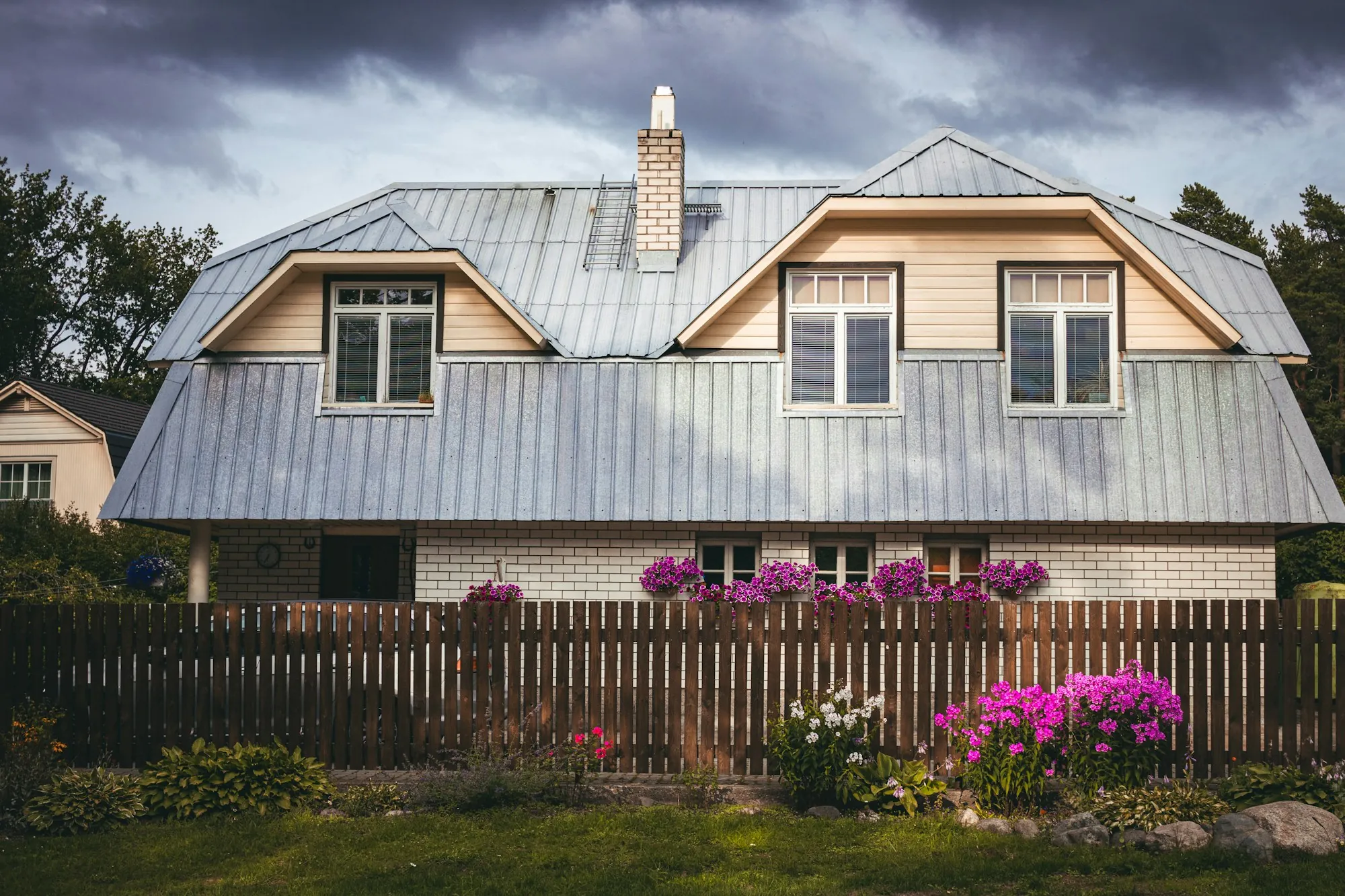 Two-story house with a silver metal roof, twin dormers and a flower garden