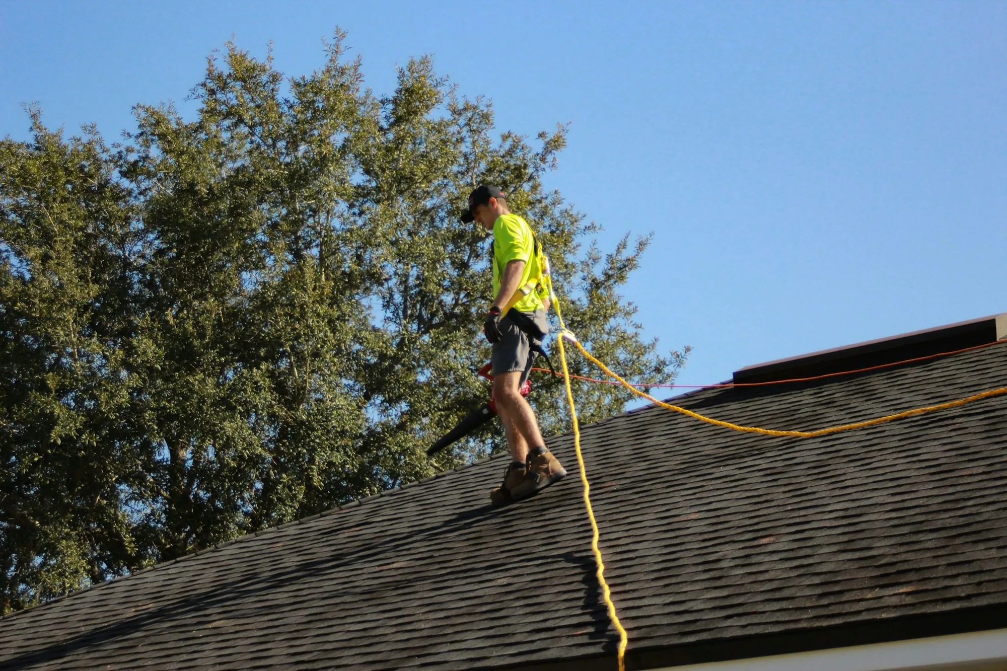 Roofer in a hi-vis shirt walking a shingle roof tied to a safety line