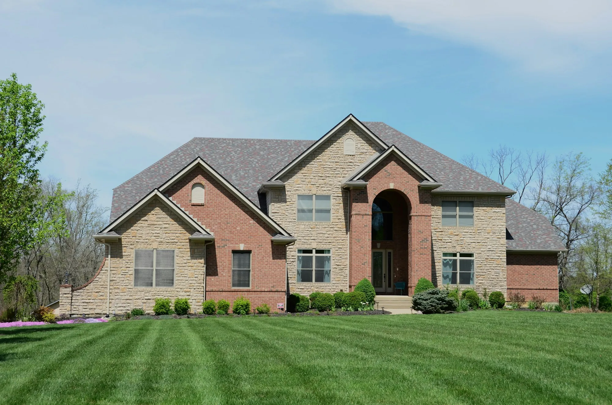 Brick and stone two-story home with a multi-gable shingle roof and striped lawn