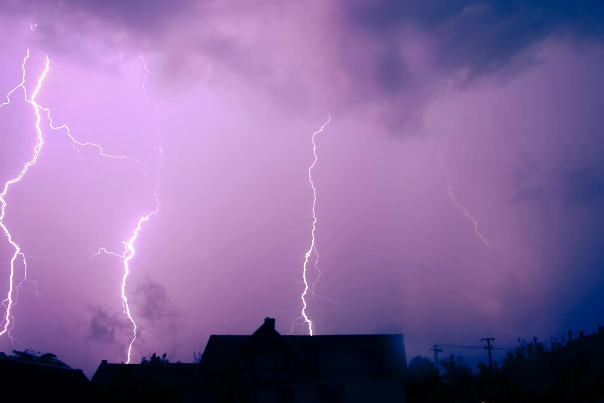 Purple night sky lit by lightning over rooftops
